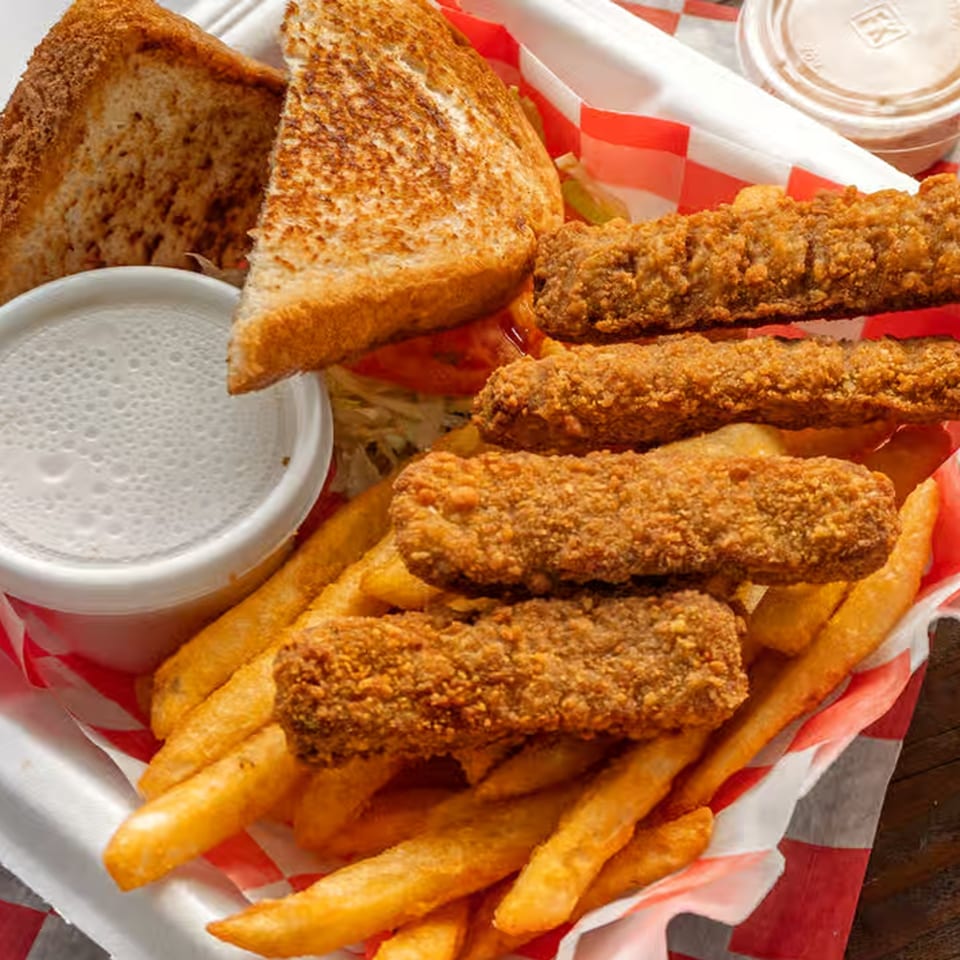 A fried steak finger basket with fries, Texas toast, and dipping sauce in a red-checkered liner.