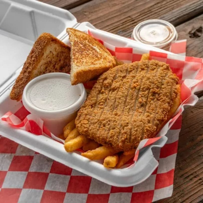Chicken fried steak, fries, and toast in a takeout container with red and white checkered paper.