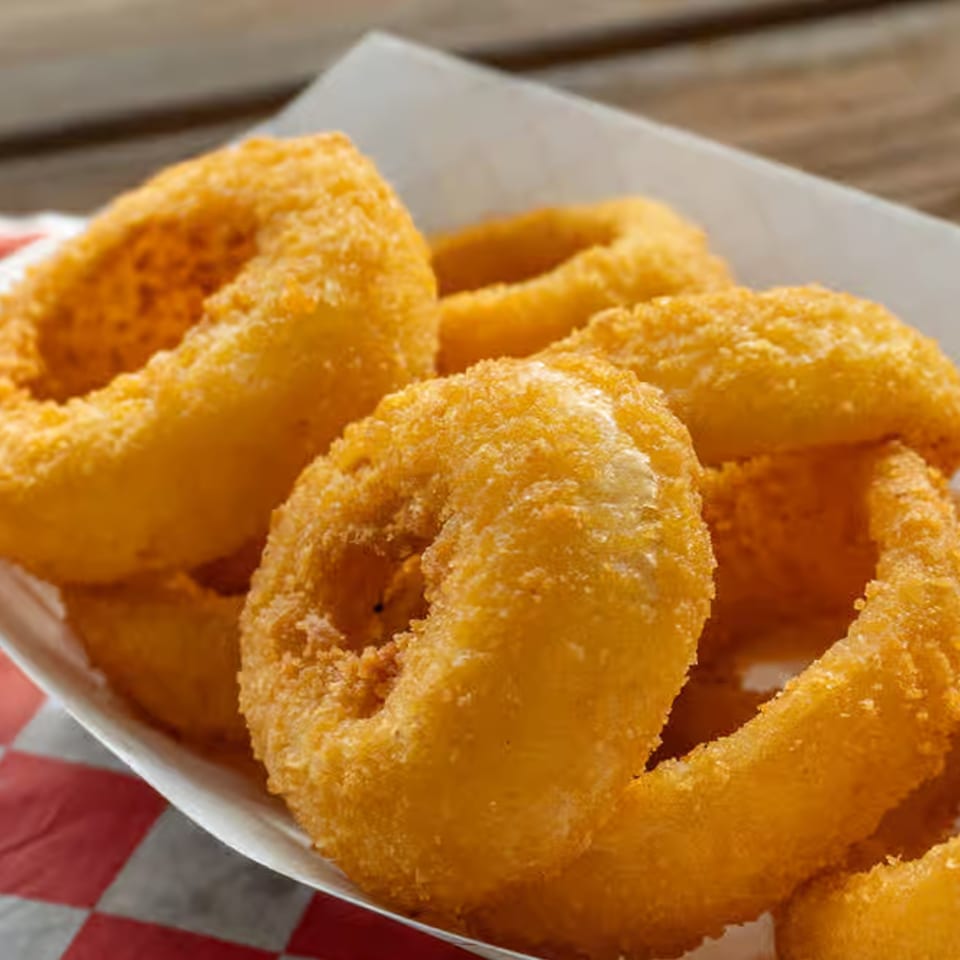 Golden-brown onion rings in a white paper tray with a red and white checkered liner.
