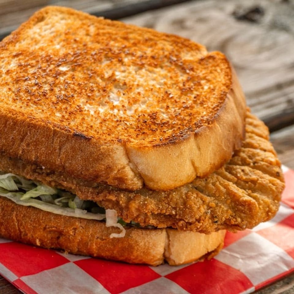 A crispy fried chicken sandwich on toasted bread with lettuce, served on red and white checkered paper.